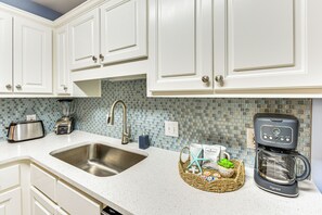 Eine Küche mit weißen Schränken, einem Edelstahl-Spülbecken, einem Toaster, einer Kaffeemaschine und einer Mosaik-Spritzschutzleiste.