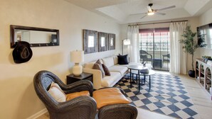 Ein Wohnzimmer mit einer Couch, Sesseln, einem Couchtisch, einem Deckenventilator, einem großen Spiegel und einem Schachbrettfußboden.