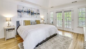 Une chambre à coucher avec un grand lit, deux tables de chevet, un tableau abstrait accroché au mur et une vue par de grandes portes-fenêtres.
