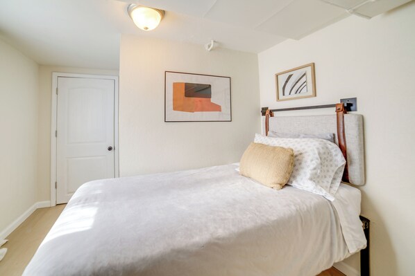 A bedroom with a bed, a door, and two framed artworks on the wall.