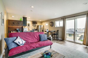 A modern living room with a red sofa, a coffee table, and a kitchen in the background. - Views of Ocean & Harbor! Quaint Gold Beach Duplex (Gold Beach)