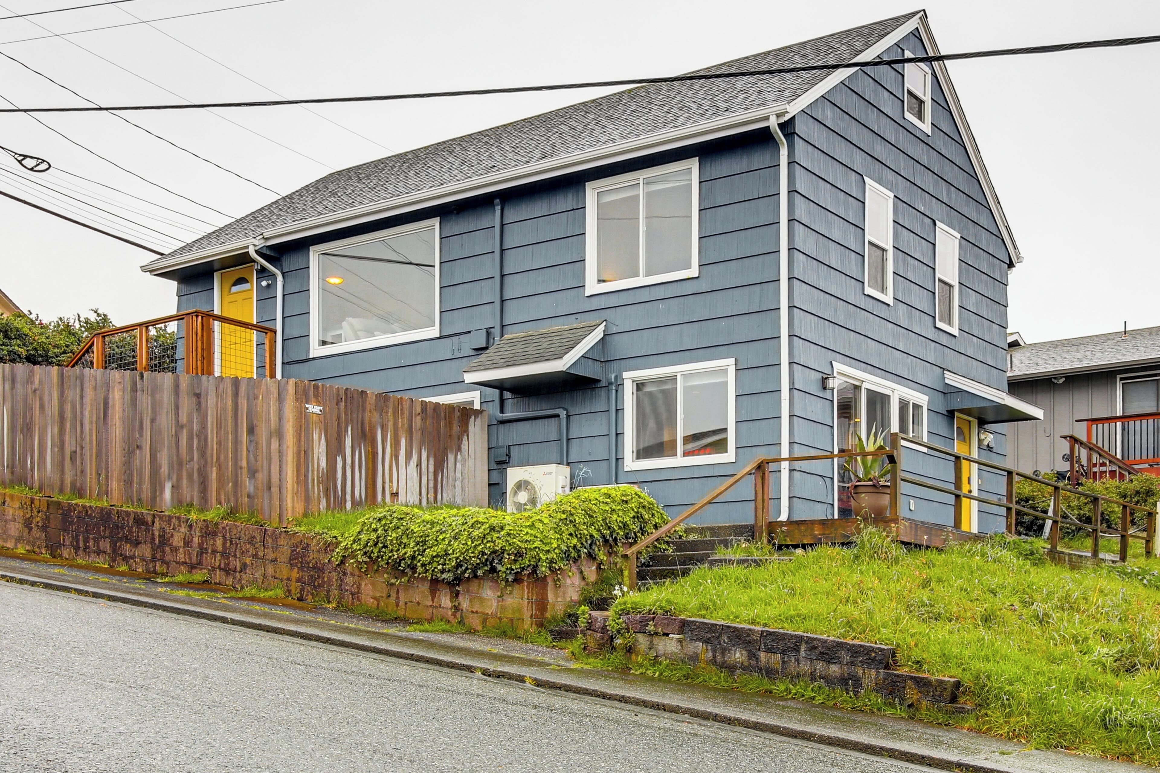 A two-story house with a front porch, a wooden fence, and a grassy yard.