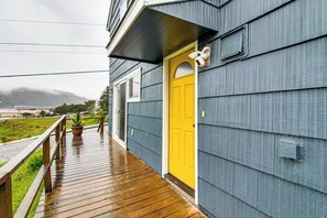 A wooden deck leading to a house with a yellow door and a white window. - Views of Ocean & Harbor! Quaint Gold Beach Duplex (Gold Beach)