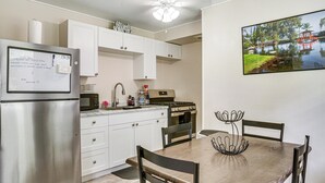 Una cocina con gabinetes blancos, un refrigerador de acero inoxidable, un microondas y una estufa a gas. Hay una mesa de comedor con sillas y un centro de mesa decorativo de metal.