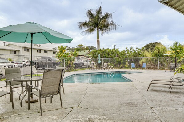 Uma área de piscina com espreguiçadeiras, uma mesa e um guarda-sol.