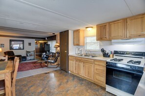 A kitchen with wooden cabinets, a stove, and a dining area with a table and chairs. - 'Elk Home' - Yellowstone Basecamp < 1 Mi to Park! (West Yellowstone)