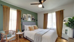 Ein Schlafzimmer mit einem Bett, einem Sessel, einem kleinen Tisch, einem Deckenventilator und einer Topfpflanze.