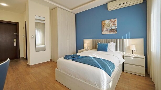 Una habitación de hotel con una cama, mesitas de noche, un espejo y un aire acondicionado.