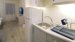 Cocina compacta con un lavamanos, refrigerador y televisor sobre una pequeña mesa.