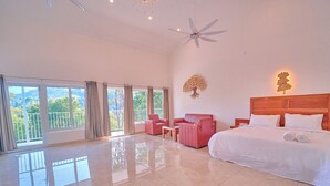 A spacious bedroom with a large bed, a ceiling fan, a nightstand, and a view of the outdoors through large windows. - Ice Cliff Munnar by VOYE HOMES (Munnar)