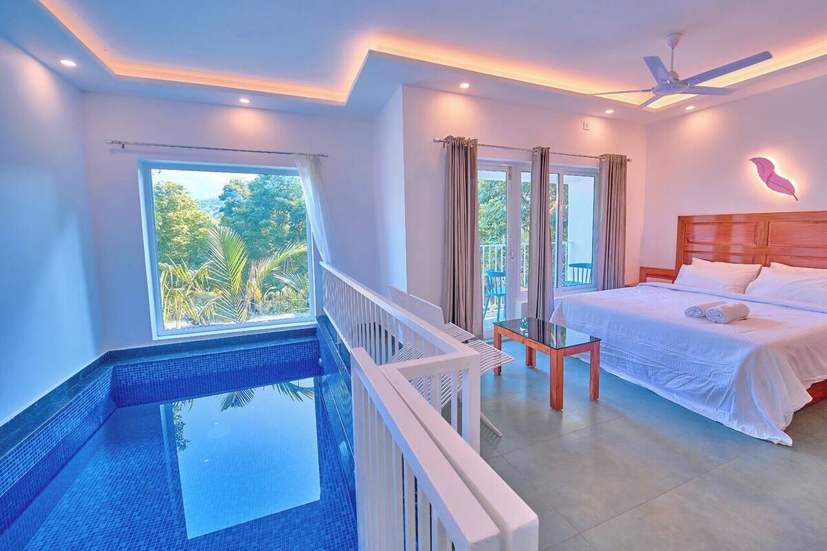 A bedroom with a large bed, a balcony, and an indoor swimming pool.