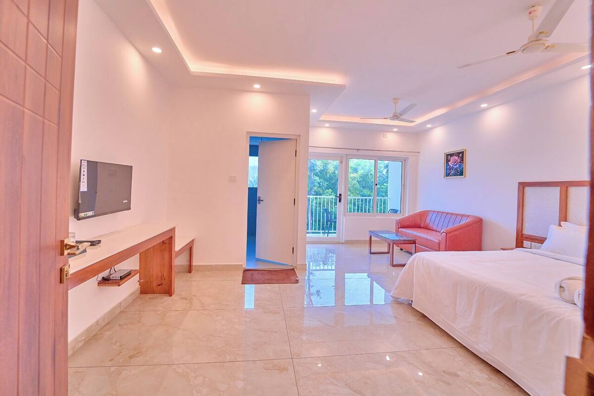 A hotel room with a bed, a TV, a balcony, and a red chair.