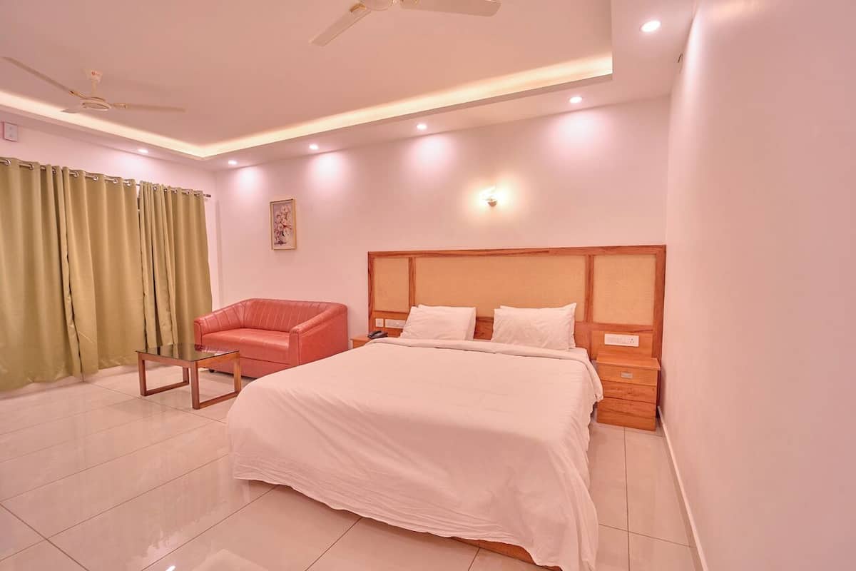 A modern hotel room with a large bed, a red armchair, a wooden nightstand, and a ceiling fan.
