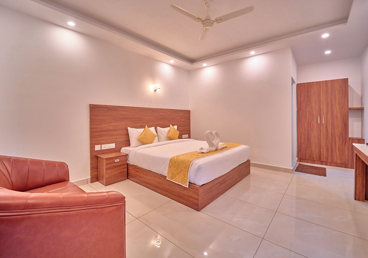 A modern bedroom with a wooden headboard, a bed with white linens and a yellow throw, a red leather sofa, and a wooden wardrobe.