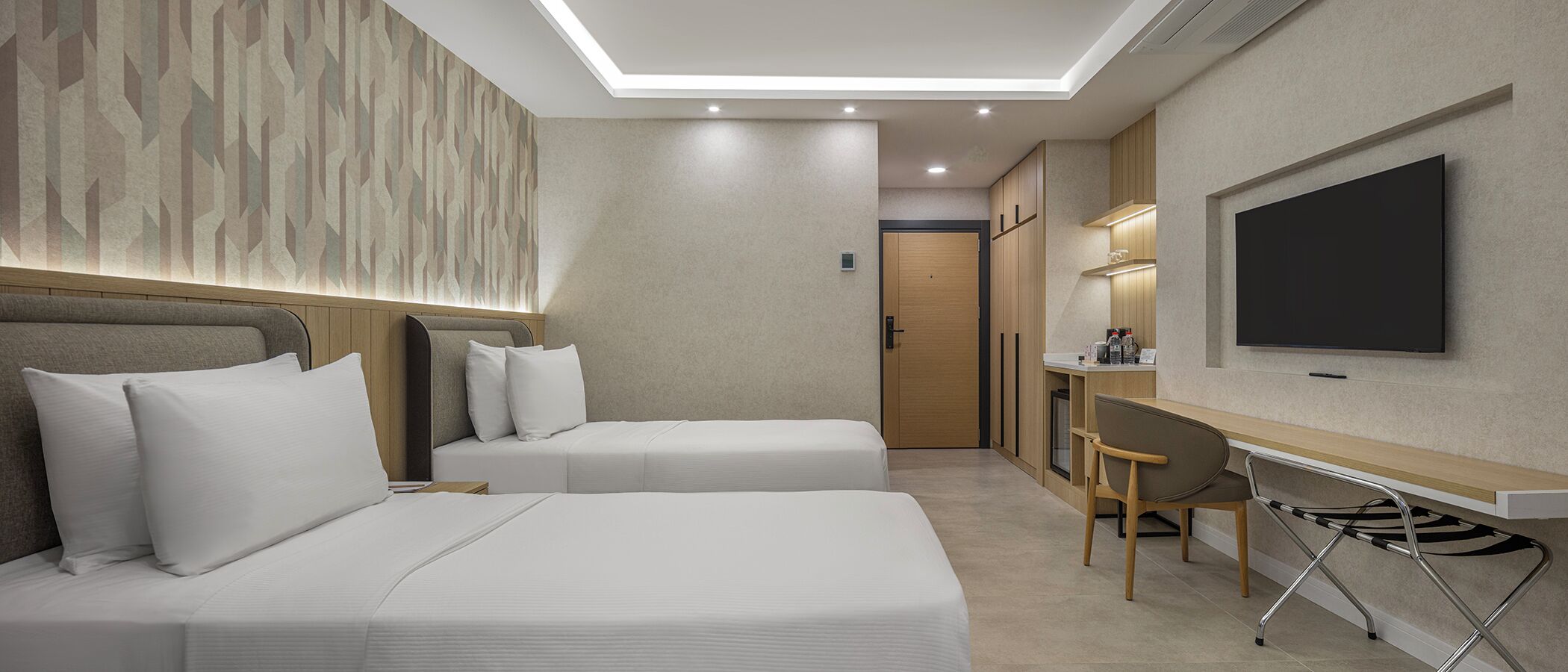 A hotel room with two beds, a desk, a chair, a TV, and a door.