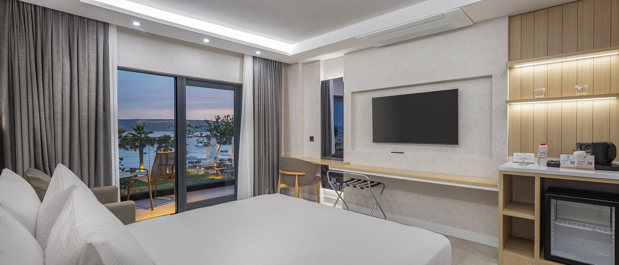Habitación de hotel con cama, escritorio, televisión y vista al mar.