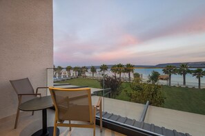 Un balcón con mesa y sillas, con vista a una playa con palmeras y cielo despejado.