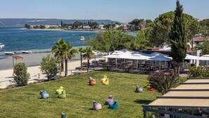 Vista costera con mesas al aire libre, playa y zona de comedor con sombrillas.