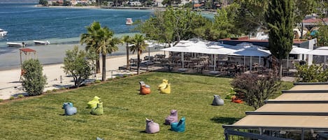 Vista costera con mesas al aire libre, playa y zona de comedor con sombrillas.