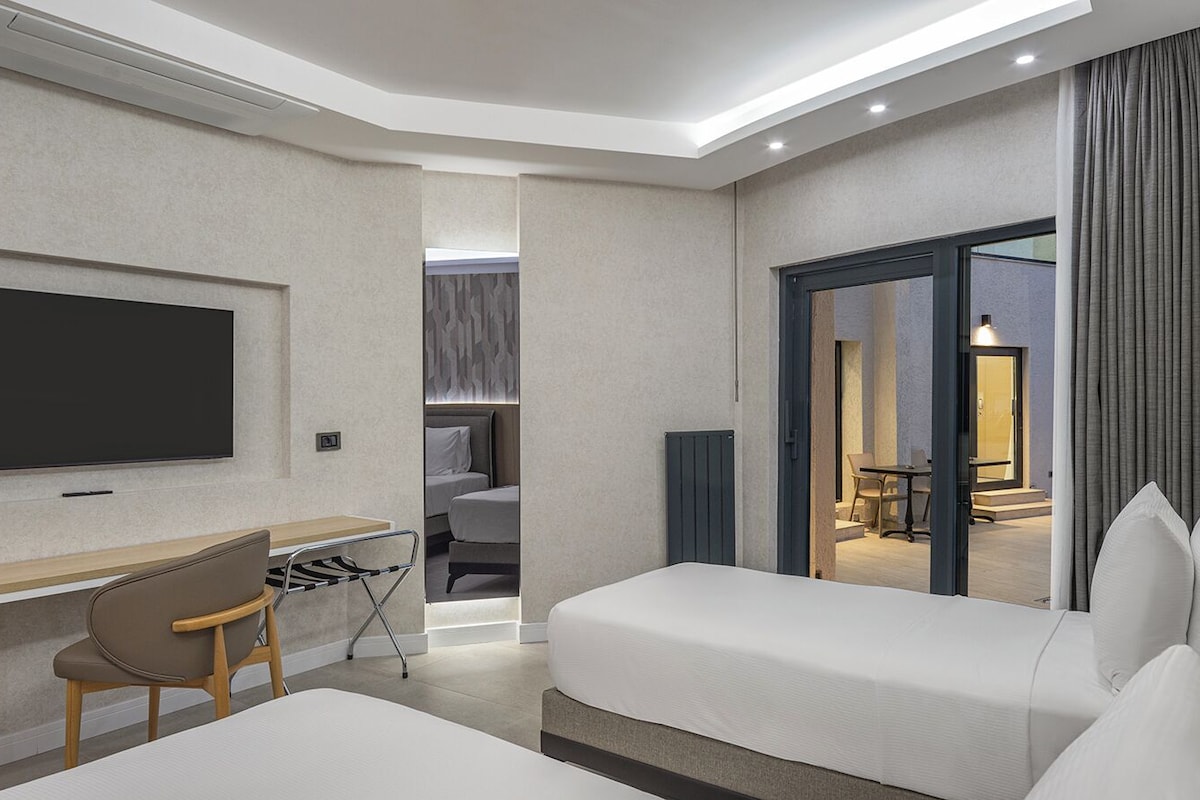 Ein modernes Hotelzimmer mit Flachbildfernseher, Schreibtisch, Stuhl, Bett und Blick ins Freie.