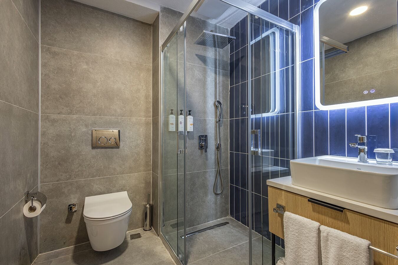 Un baño moderno con ducha de vidrio, inodoro blanco y lavabo con espejo superior.
