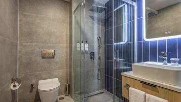 Un baño moderno con ducha de vidrio, inodoro blanco y lavabo con espejo superior.