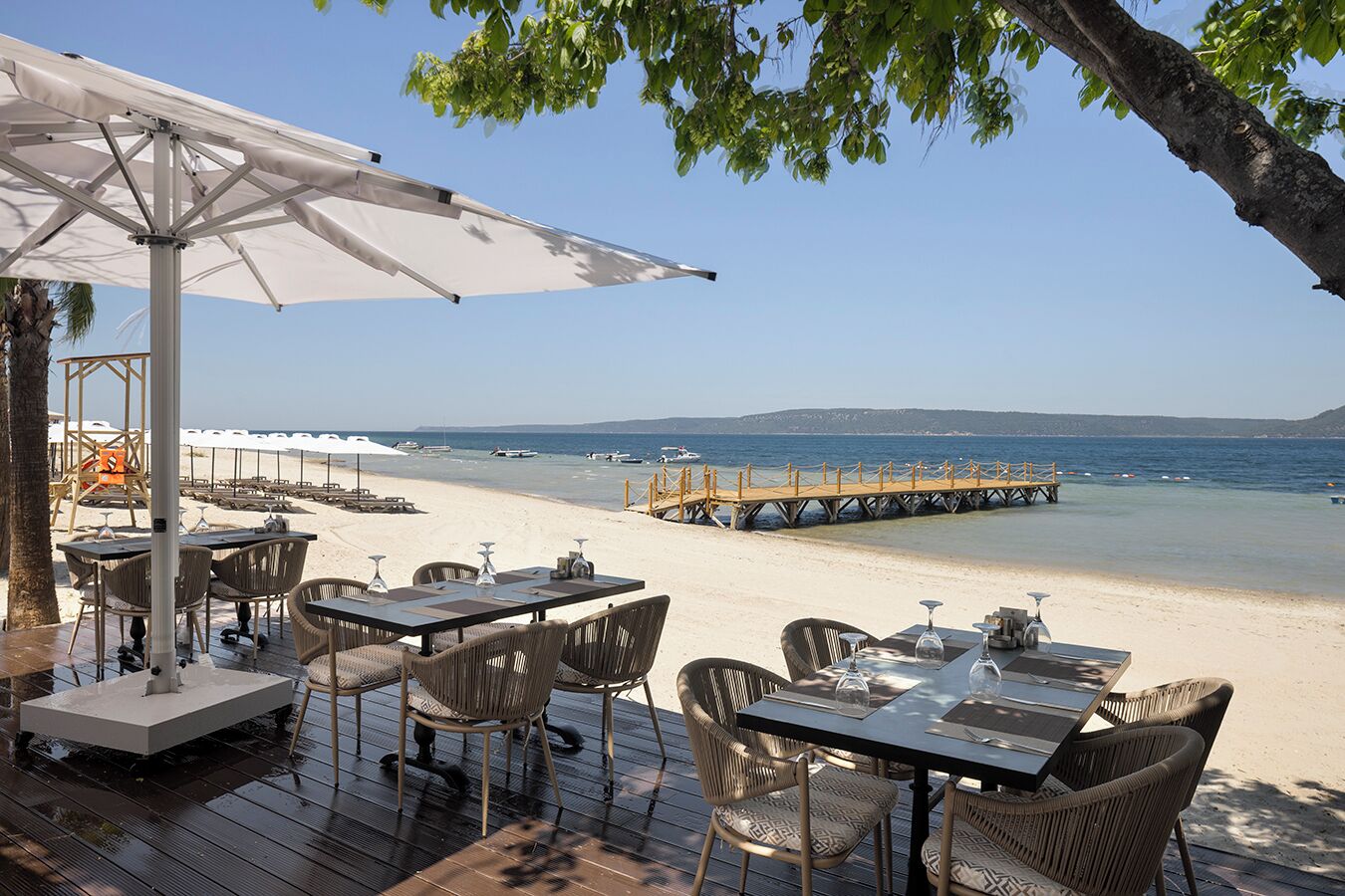 Un área de comedor al aire libre con mesas y sillas, una torre de salvavidas y un muelle de madera que se adentra en el mar.