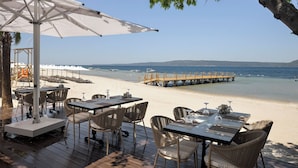 An outdoor dining area with tables and chairs, a lifeguard tower, and a wooden pier extending into the sea. - The Komana Dardanelles (Çanakkale)