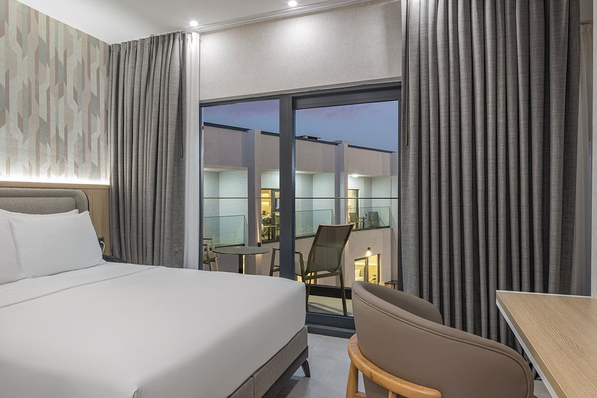 Une chambre d’hôtel comprenant un lit, un bureau, une chaise et un balcon avec une porte vitrée.