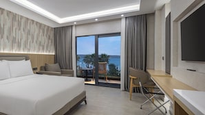 Habitación de hotel con cama, escritorio, silla, televisor y balcón con vistas.