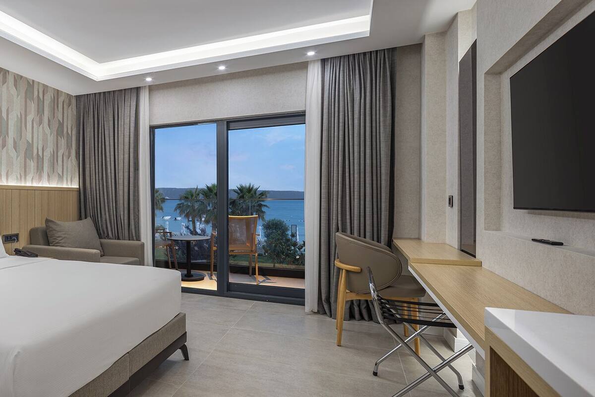 A hotel room with a bed, a desk, a chair, a TV, and a balcony with a view.
