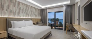 Ein Hotelzimmer mit einem Bett, einem Schreibtisch, einem Sessel, einem Fernseher und einem Balkon mit Blick.