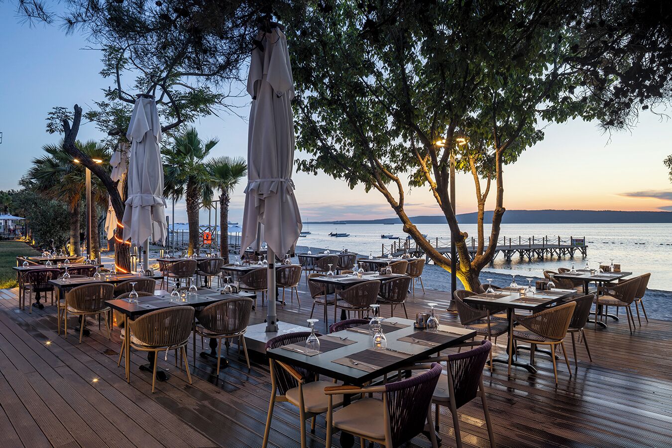Un área de comedor al aire libre con mesas, sillas, sombrillas y vistas al mar.