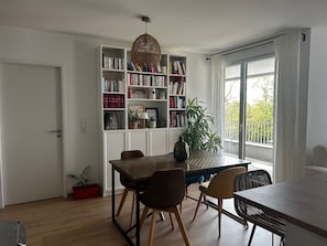 Un coin repas comprenant une table en bois, des chaises, une bibliothèque et un luminaire suspendu.