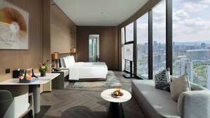Una habitación de hotel moderna con cama, sofá, mesa de comedor y un amplio ventanal con vista a la ciudad.