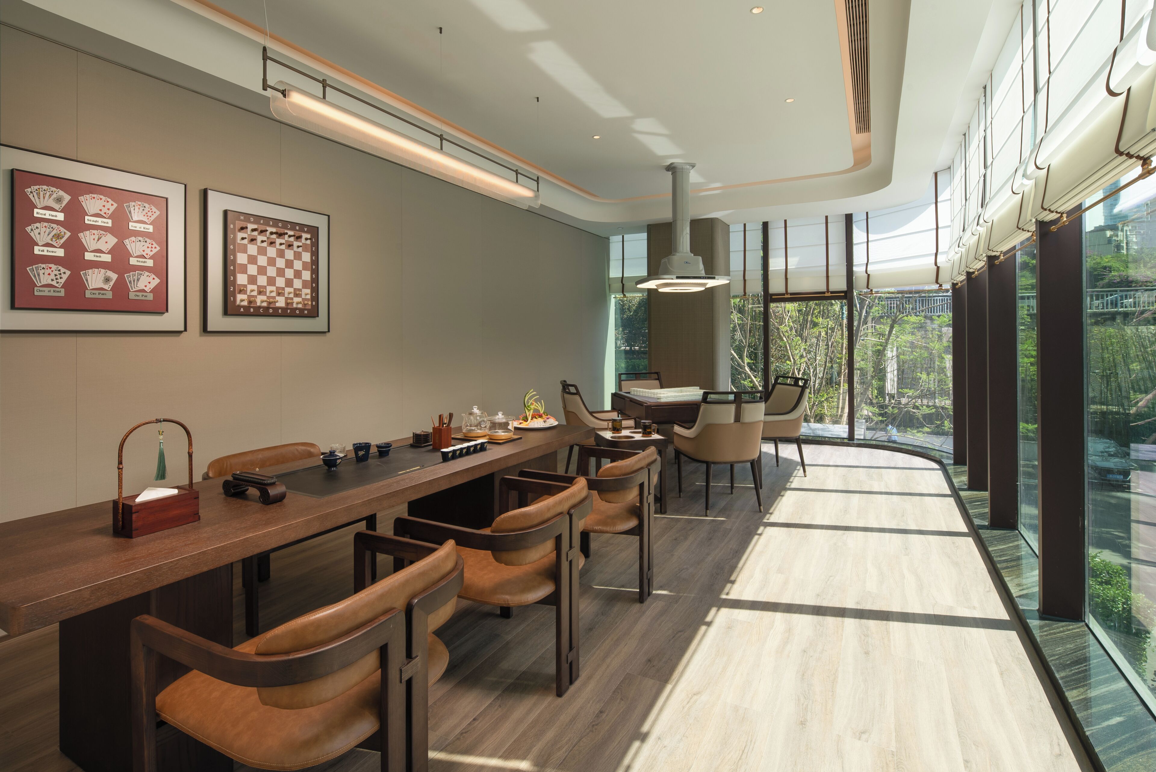 A modern dining area with a long wooden table, leather chairs, and framed chess and playing card sets on the wall.