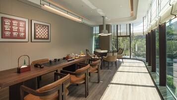 A modern dining area with a long wooden table, leather chairs, and framed chess and playing card sets on the wall.