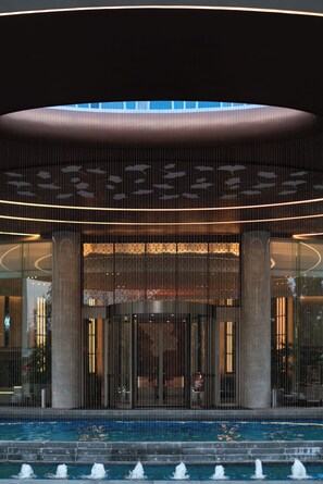 A modern hotel entrance with a pool, large columns, and a glass facade.