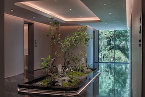 A modern lobby with a glass partition, a reception desk, and a large window offering a view of greenery.