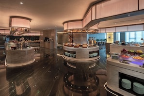A modern hotel lobby with a central round bar area, seating, and a view of the city.
