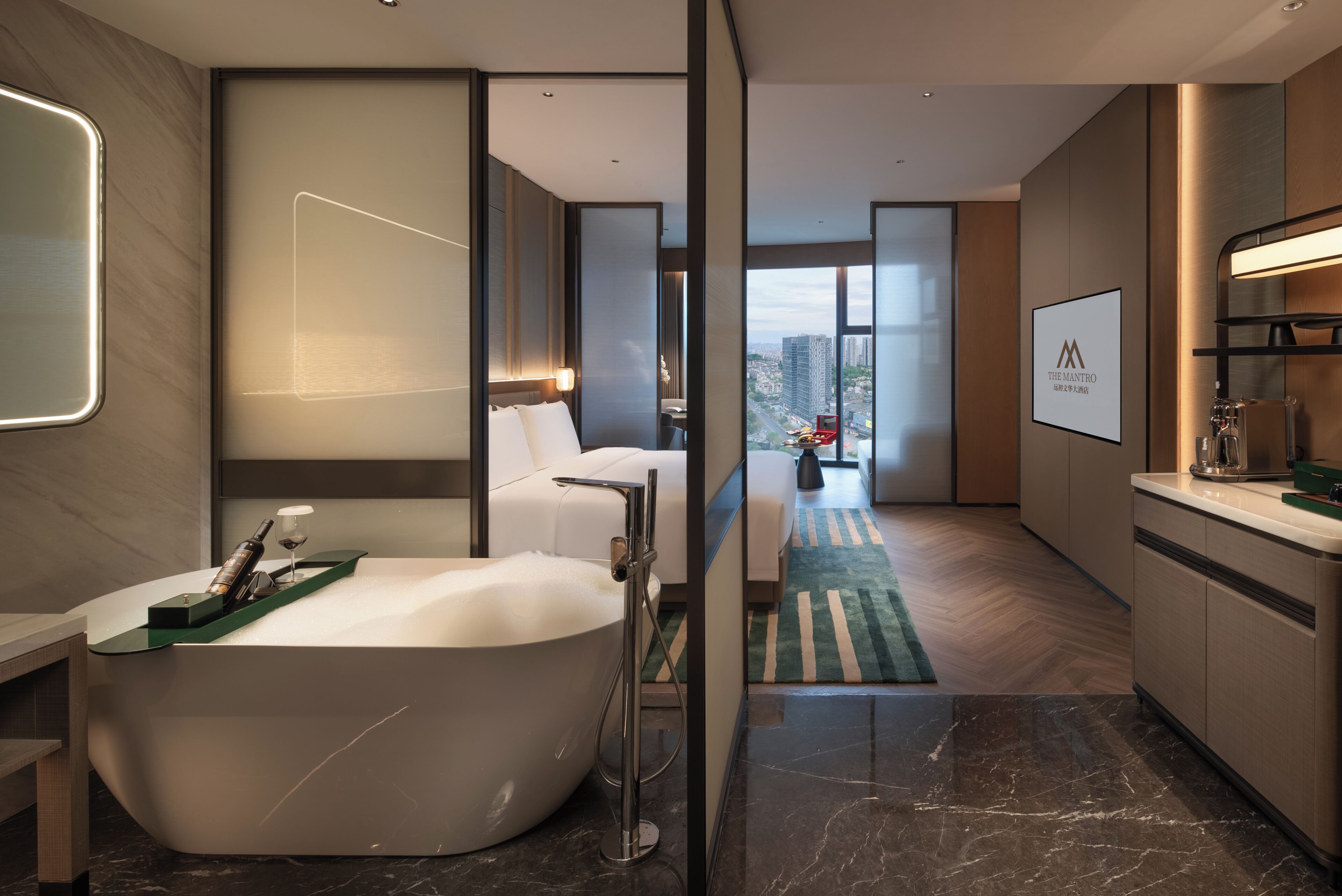Un baño de hotel moderno con una bañera independiente, un espejo grande y vistas a la ciudad.