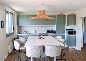 A modern kitchen with a central island, bar stools, and a hanging light fixture. - Le Pivoine : vue mer à La Baule (La Baule-Escoublac)