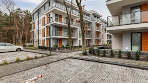 A multi-story residential building with balconies, a car in the driveway, and a gravel pathway. - Comfortable Apartment | Pool | Close to the Beach (Pobierowo)
