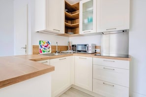 A modern kitchen with white cabinets, a wooden countertop, a microwave, a toaster, and a sink. - Le Joli Baulois - La Baule (La Baule-Escoublac)