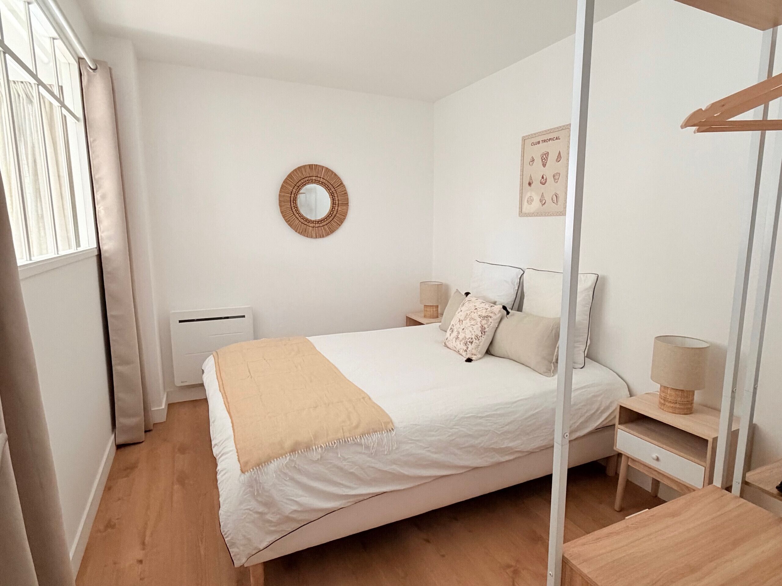 A bedroom with a bed, bedside tables, a mirror, a radiator, and a window with curtains.