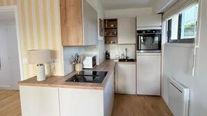 Uma cozinha moderna com micro-ondas embutido, forno e frigorífico, armários de madeira e parede riscada.