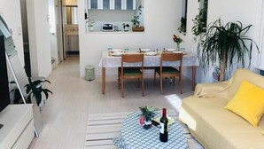 A modern living room with a sofa, a dining table with chairs, a TV, and a kitchen area in the background. - Takara House (Tokyo)