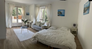 Ein Schlafzimmer mit einem großen Bett, zwei Nachttischen, einem kleinen Tisch mit Blumen und einem Fenster mit Vorhängen.