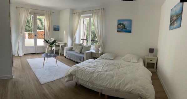 Une chambre à coucher avec un grand lit, deux tables de chevet, une petite table ornée d’un vase de fleurs et une fenêtre avec des rideaux.