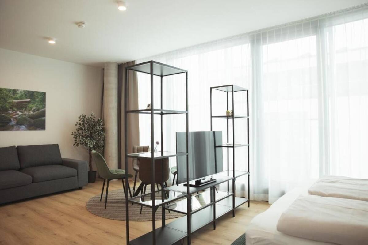 Ein modernes Hotelzimmer mit Sofa, Fernseher auf einem Schrank, Esstisch mit Stühlen und einem Bett.